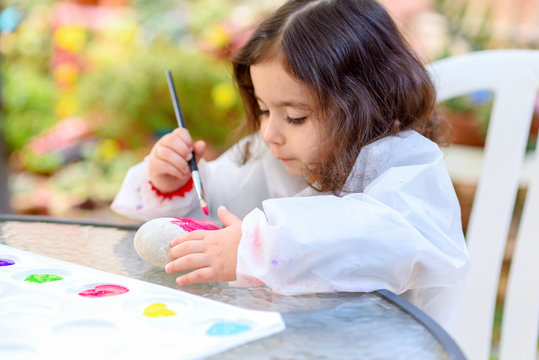 Portrait of little child painting, summer outdoor.Kid drawing on a stone.