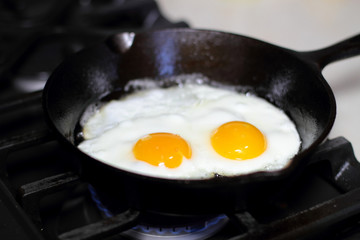 Two eggs frying sunny-side up in a cast iron pan on the stove.