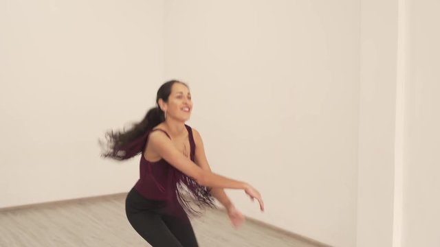 An extremely beautiful female dancer makes various latino moves. She practices freestyle, tries arm and body waves, puts her arm down and up, together and separately, rolls, smiles and have fun.