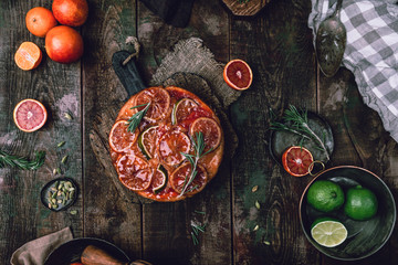 Obraz na płótnie Canvas citrus upside down cake with blood oranges, lemons and limes on wooden board among fresh citrus fruit, kitchen stuff, herbs and spices on old wooden background, toned for a vintage effect