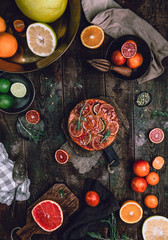 Fototapeta na wymiar citrus upside down cake with blood oranges, lemons and limes on wooden board among fresh citrus fruit, kitchen stuff, herbs and spices on old wooden background, toned for a vintage effect