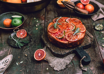 citrus upside down cake with blood oranges, lemons and limes on wooden board among fresh citrus fruit, kitchen stuff, herbs and spices on old wooden background, toned for a vintage effect