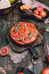 citrus upside down cake with blood oranges, lemons and limes on wooden board among fresh citrus fruit, kitchen stuff, herbs and spices on old wooden background, toned for a vintage effect