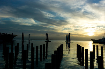 old wooden pier at sunrise with racing sailboat by the bay