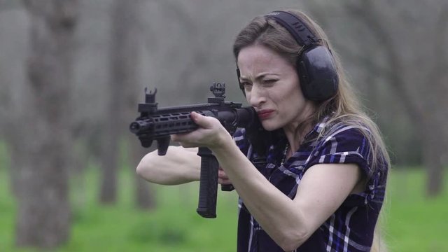 Front view of a woman getting recoil from firing a weapon multiple times at a target, slow motion 24fps.