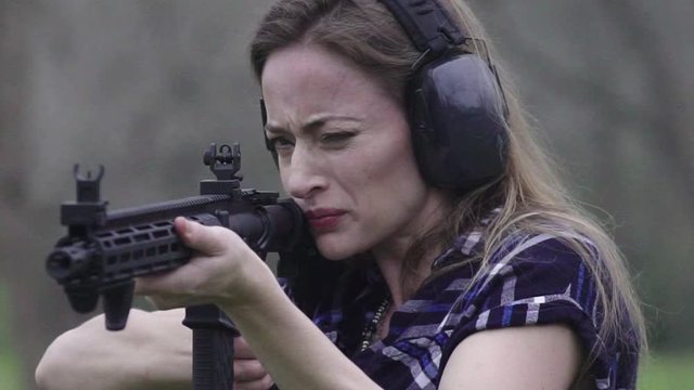 Close up view in front of a woman getting recoil from firing a weapon multiple times at a target, slow motion 24 fps.