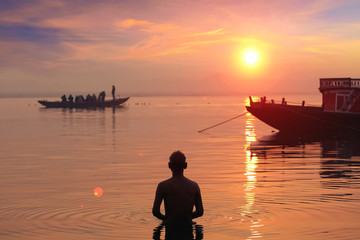 Old man meditates and offer prayers standing near the Ganges river bank at Varanasi at sunrise