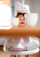 A portrait of small girl in unicorn mask sitting at the table at home.