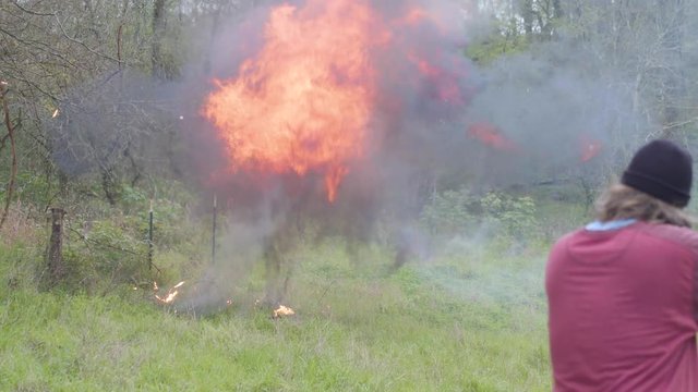 Insane man shooting bomb, huge flames from explosion in rural scene 4k