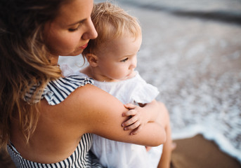 Close-up of young mother with a toddler girl on beach on summer holiday.