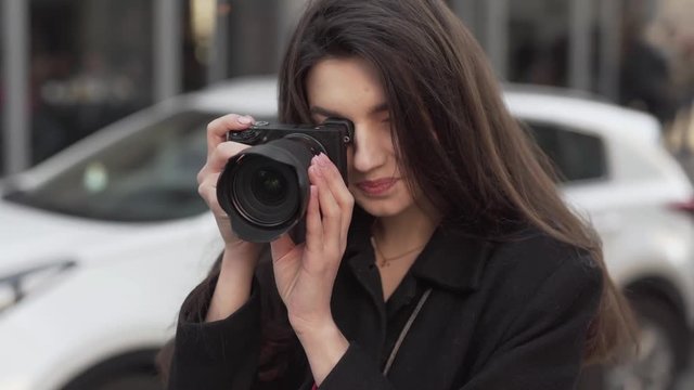 Close up of a beautiful female photographer smiling while taking pictures in a city.