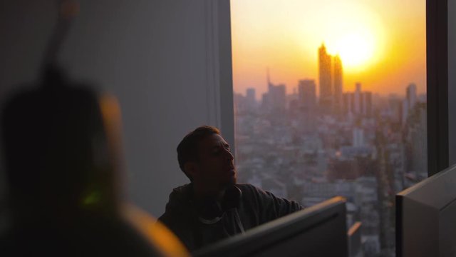 SLOW MOTION: Still shot of Software developers working in their Bangkok office during a vibrant colurful sunset, which creates a sillouette. A relaxed young entrepeneur environment.