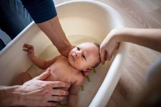 Unrecognizable parents giving a newborn baby a bath at home.
