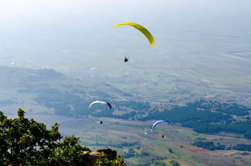 Three paraglider flies paraglider over the tops of the mountains in summer sunny day