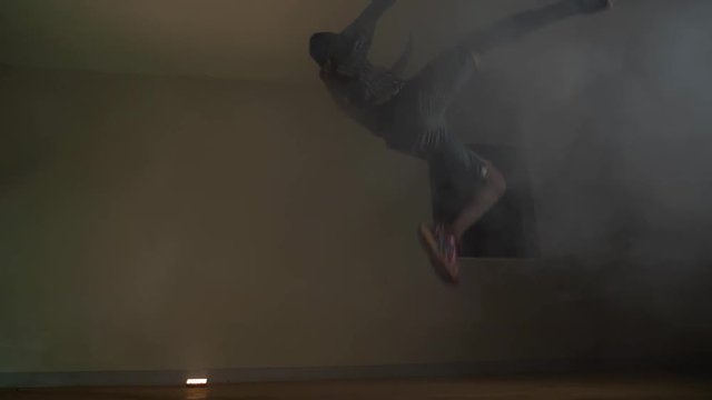 Slow motion shot of African youth in a beanie doing a very large kick jump and spin in the air in colorful disco lights and smoke.