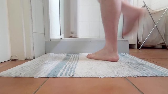 Man having a shower in his home. Close up shot of his feet getting into the shower.