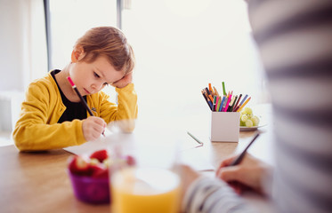 Unrecognizable mother with small daughter drawing in a kitchen.