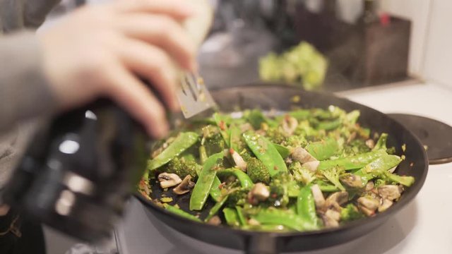 Woman cooking wok with mushrooms, brocolli, chili, noodles, leek, suger peas and soy.