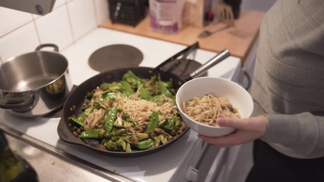 Woman cooking wok with mushrooms, brocolli, chili, noodles, leek, suger peas and soy.