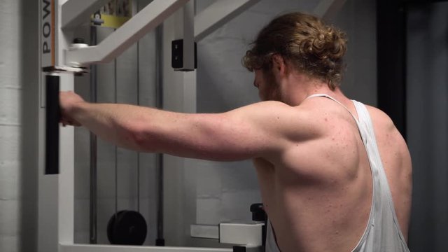 Young bearded ginger male training rear (back) shoulders hard on a pec deck in an old, rusty Arnold era gym (Gold's Gym) close-up