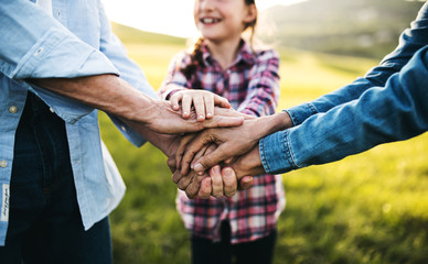 Hands of small girl and her senior grandparents on top of each other outside.