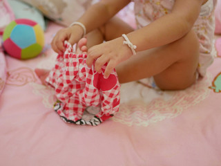 Selective focus on little Asian baby girl's hands holding on short pants, as she learning to put it on by herself - child development by allowing them to do things by themselves