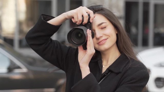 A head and shoulder close up video of a beautiful girl with amazing smile and long dark hair. She holds a camera and tries to take photos from different angles. The background is blurred.