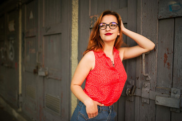 Attractive redhaired woman in eyeglasses, wear on red blouse and jeans skirt posing.