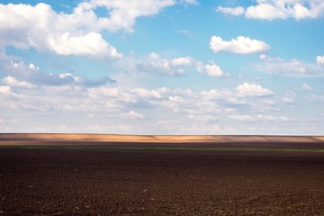 Fototapeta premium Landscape of arable land fields. Countryside plowed land with hills in distance and blue sky with clouds. Agriculture fields landscape.