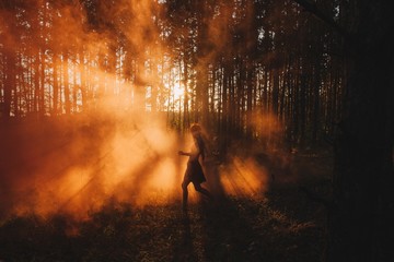 Silhouette of girl walking by fog in sunset light in pine forest