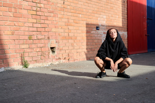 Teen girl in hood sitting on her haunches.