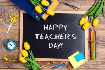 Flat lay composition for Teacher's day on chalkboard with school supplies and tulip flowers on a rustic wooden table.