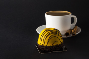 Mango sweet cake. White cup of hot coffee and Cinnamon sticks isolated on black background.