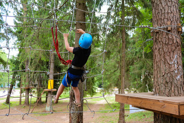 child in equipment (helmet, safety rope)  has challenge high up the rope climbing  with safety system in an adventure park 