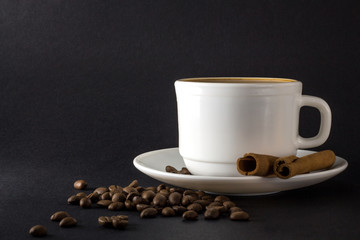 White cup of hot coffee and Cinnamon sticks isolated on black background.