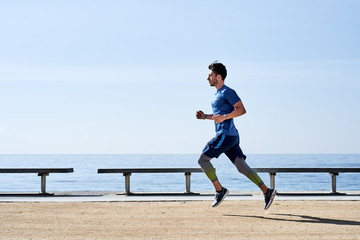 Strong athlete running on sunny embankment