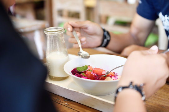 Couple sharing a healthy breakfast bowl of tropical fruit, granola and coconut smoothie