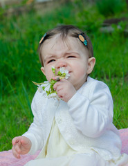 Baby in bright clothes on a pink plaid on green grass in the park. Newborn baby outside on a warm day. Little girl plays on a plaid on a green lawn in spring