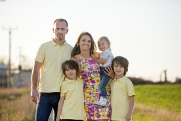 Beautiful family, mother, father and three kids, boys, having familly outdoors portrait taken on a sunny spring evening, beautiful blooming garden, sunset time
