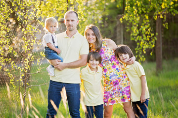 Beautiful family, mother, father and three kids, boys, having familly outdoors portrait taken on a sunny spring evening, beautiful blooming garden, sunset time