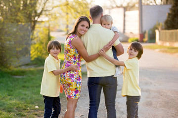 Fototapeta premium Beautiful family, mother, father and three kids, boys, having familly outdoors portrait taken on a sunny spring evening, beautiful blooming garden, sunset time