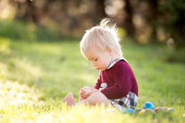 Sweet toddler boy with bunny ears, egg hunting for Easter, child and Easter day traditions