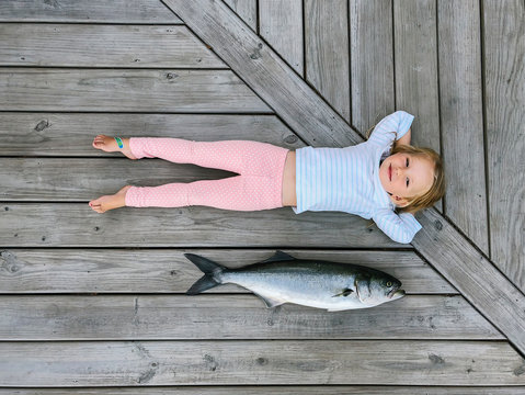 Girl Lying Next to Bluefish that Fisherman Caught that afternoon