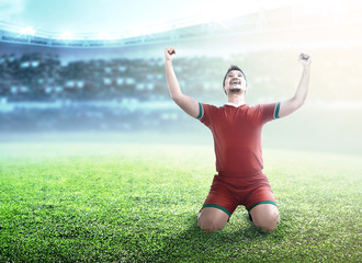 Fototapeta na wymiar Football player man celebrate his goal with raised arms and kneeling