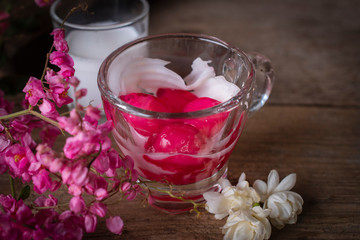 Thapthim krop, mock pomegranate seeds in coconut and syrup in the glass on the wood table there are flower and coconut milk placed around.