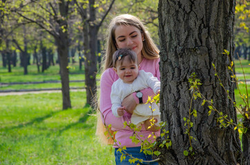 Mom with baby in bright clothes on a pink plaid on the green right. Family resting in the park on a warm day. Mom and little girl 10 months walk in the park