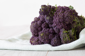 Purple sprouting broccoli bunch on a green tea towel with a grey wood background