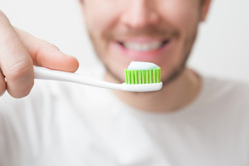 Young bearded man in t-shirt holding white toothbrush with green bristles with toothpaste. Daily...