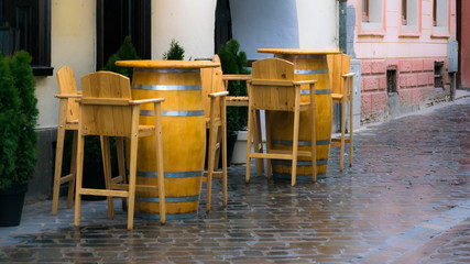 empty wooden chairs and tables barrels on street on rainy day