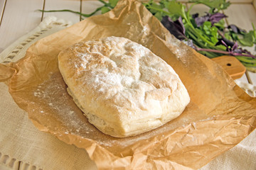 Ciabatta italian white bread on parchment paper on a wooden table, next to fresh greens and cotton napkin.View from above